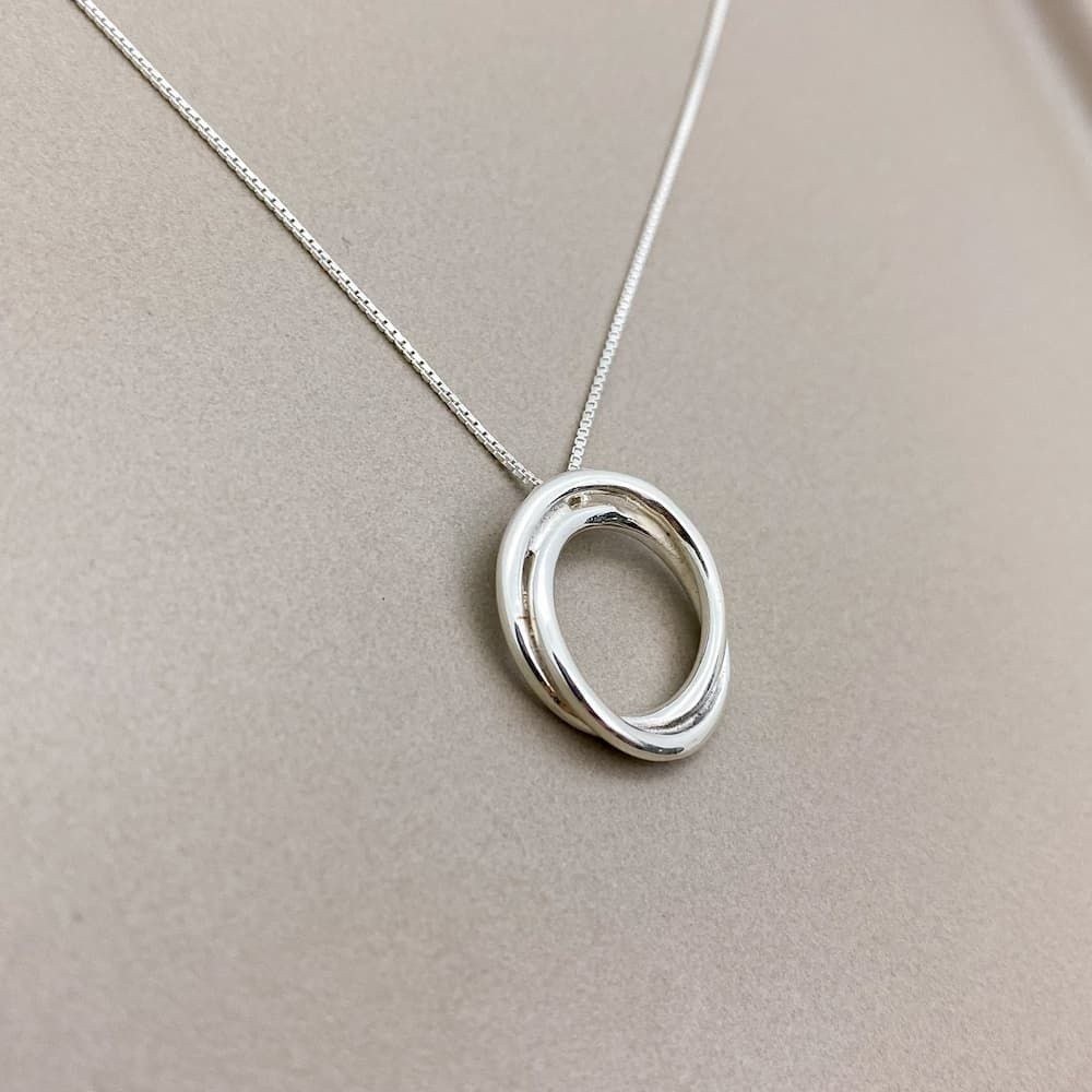 Foto próxima do Colar de prata Nó de Marinheiro sobre uma superfície lisa de cor escura