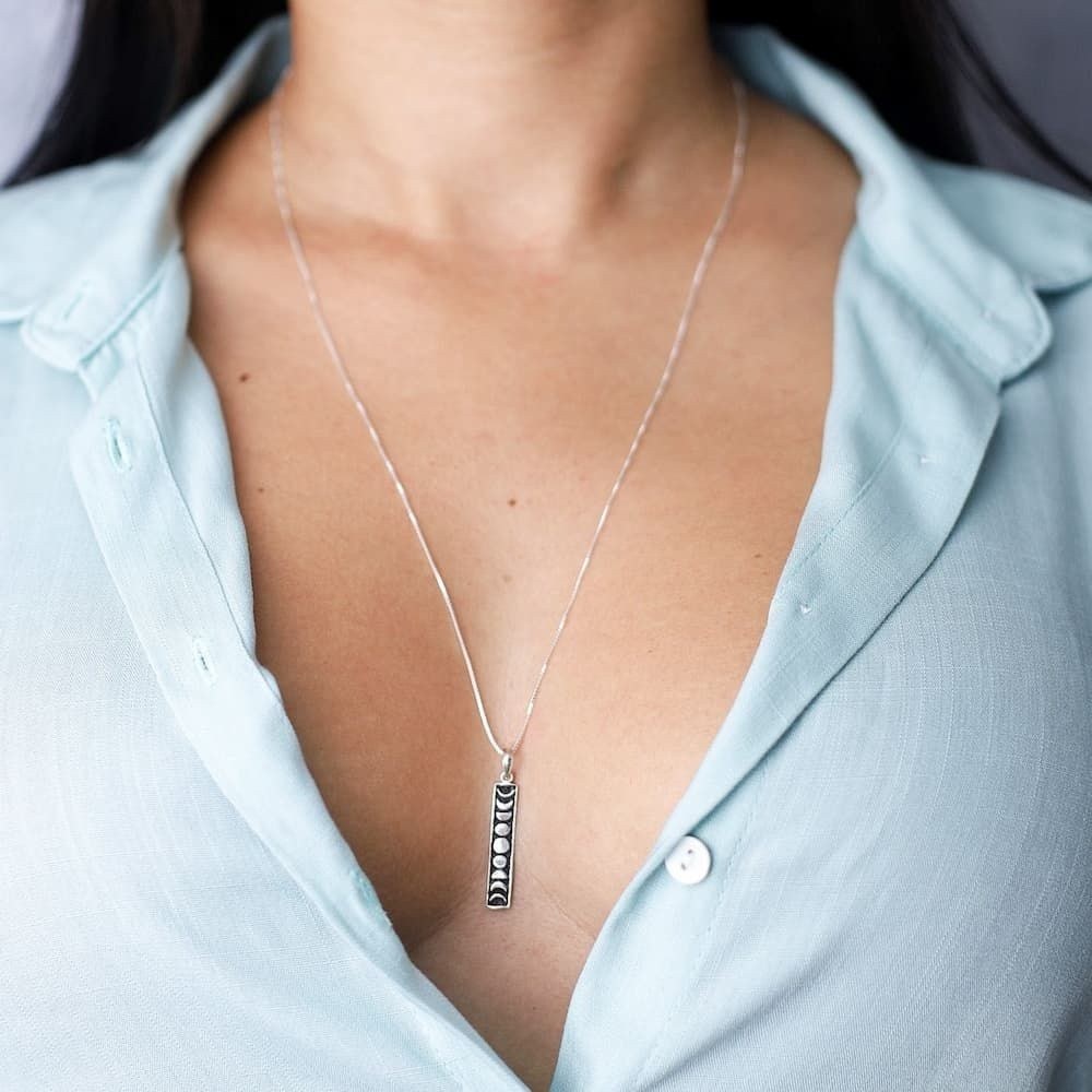 Moça jovem de blusa azul usando um colar Fases da Lua