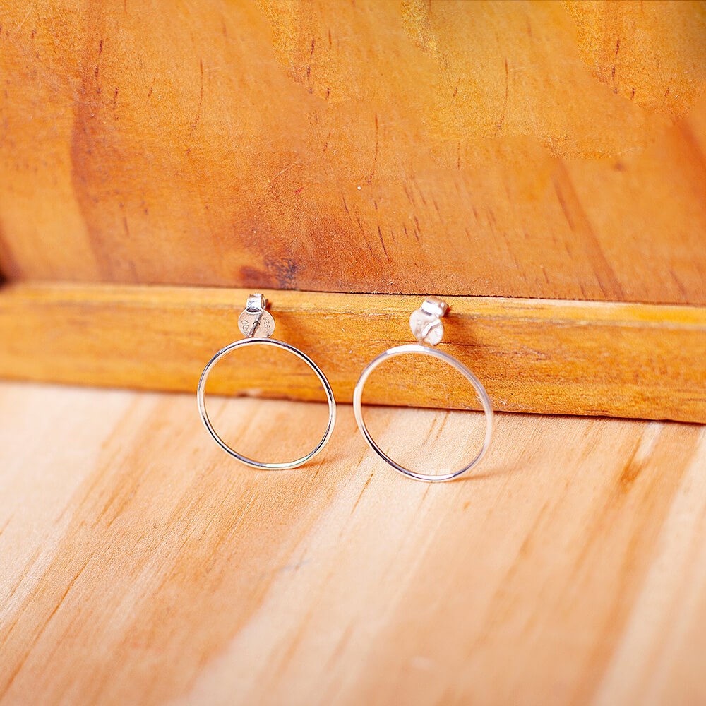 Foto do Brinco Circulo tamanho M apoiado em uma base de madeira rústica