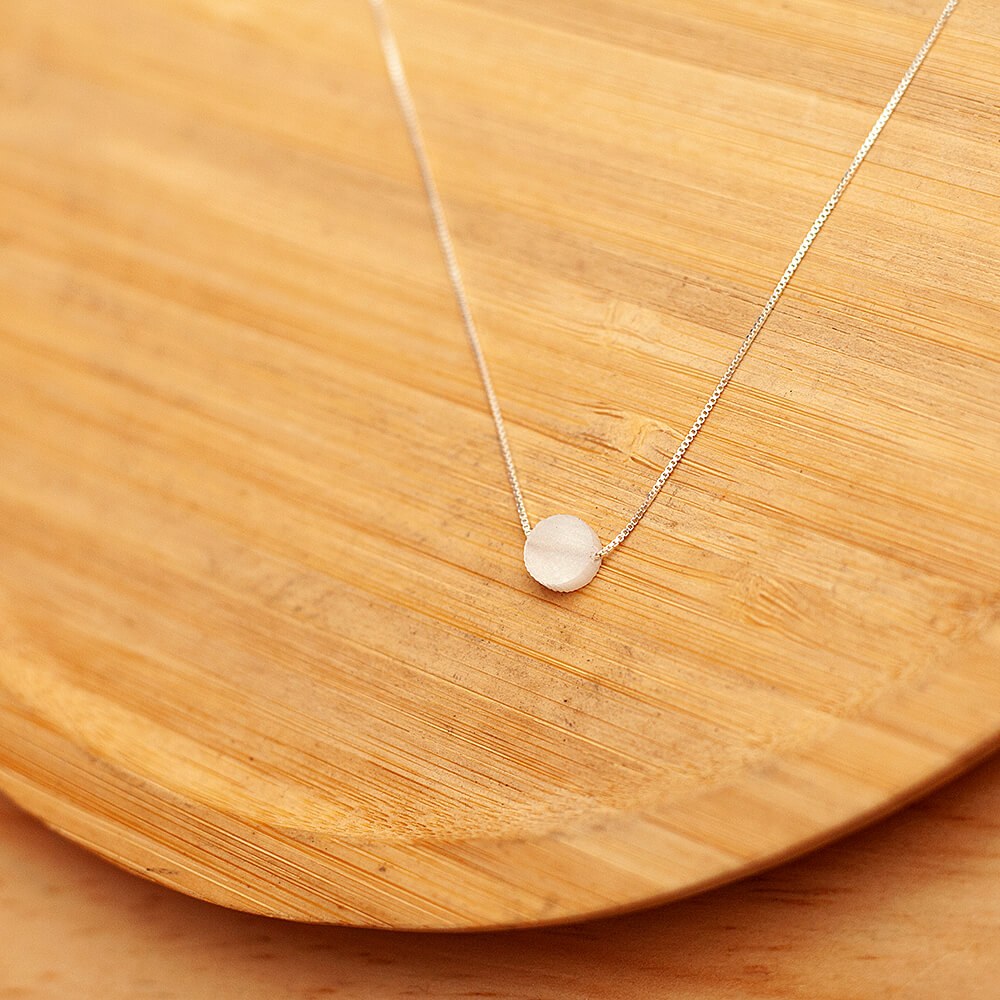 Foto do colar “Choker Madreperola”, acima de uma base de madeira rústica