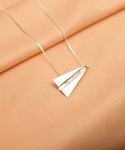 Foto do colar “Avião de Papel”, acima de uma base de tecido