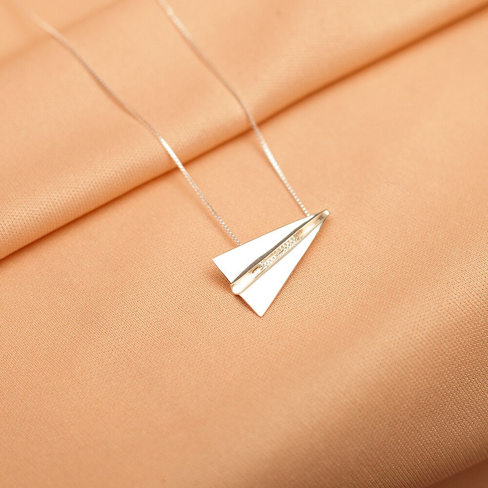 Foto do colar “Avião de Papel”, acima de uma base de tecido