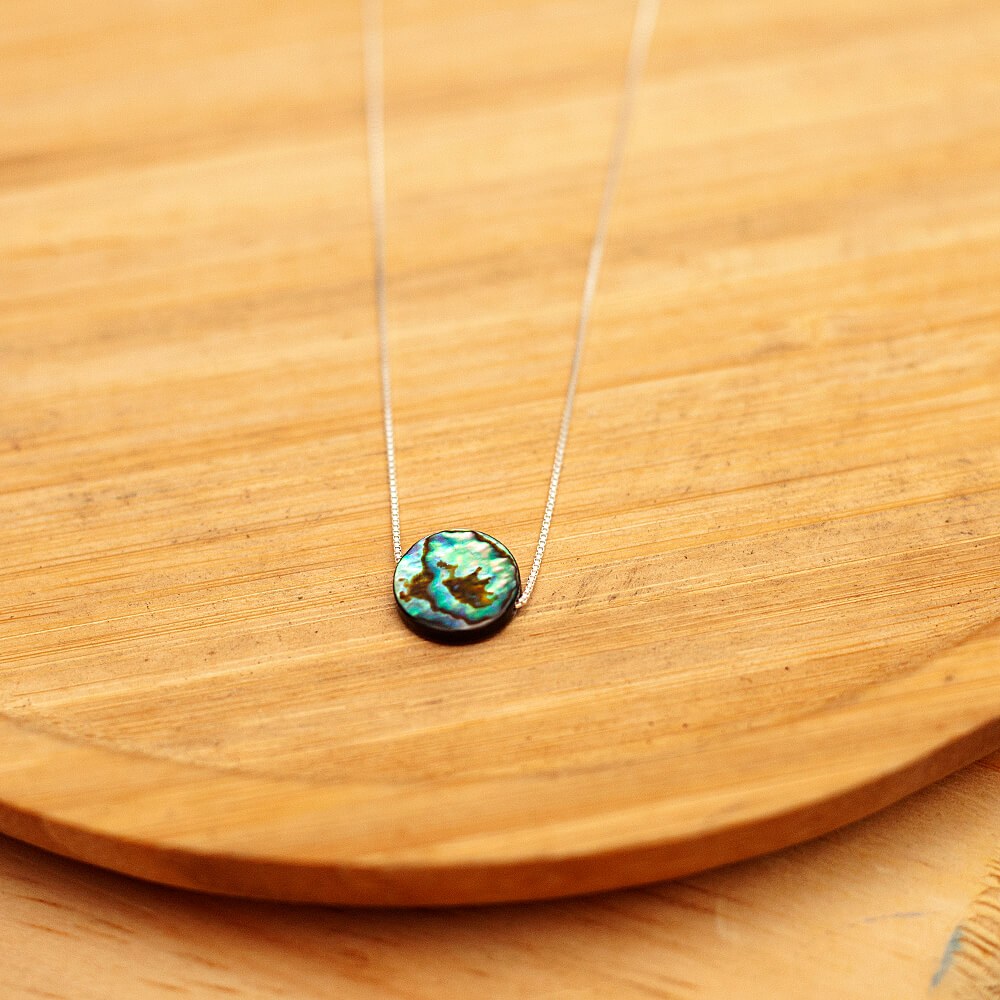 Foto do colar “Circulo Abalone”, acima de uma base de madeira rústica