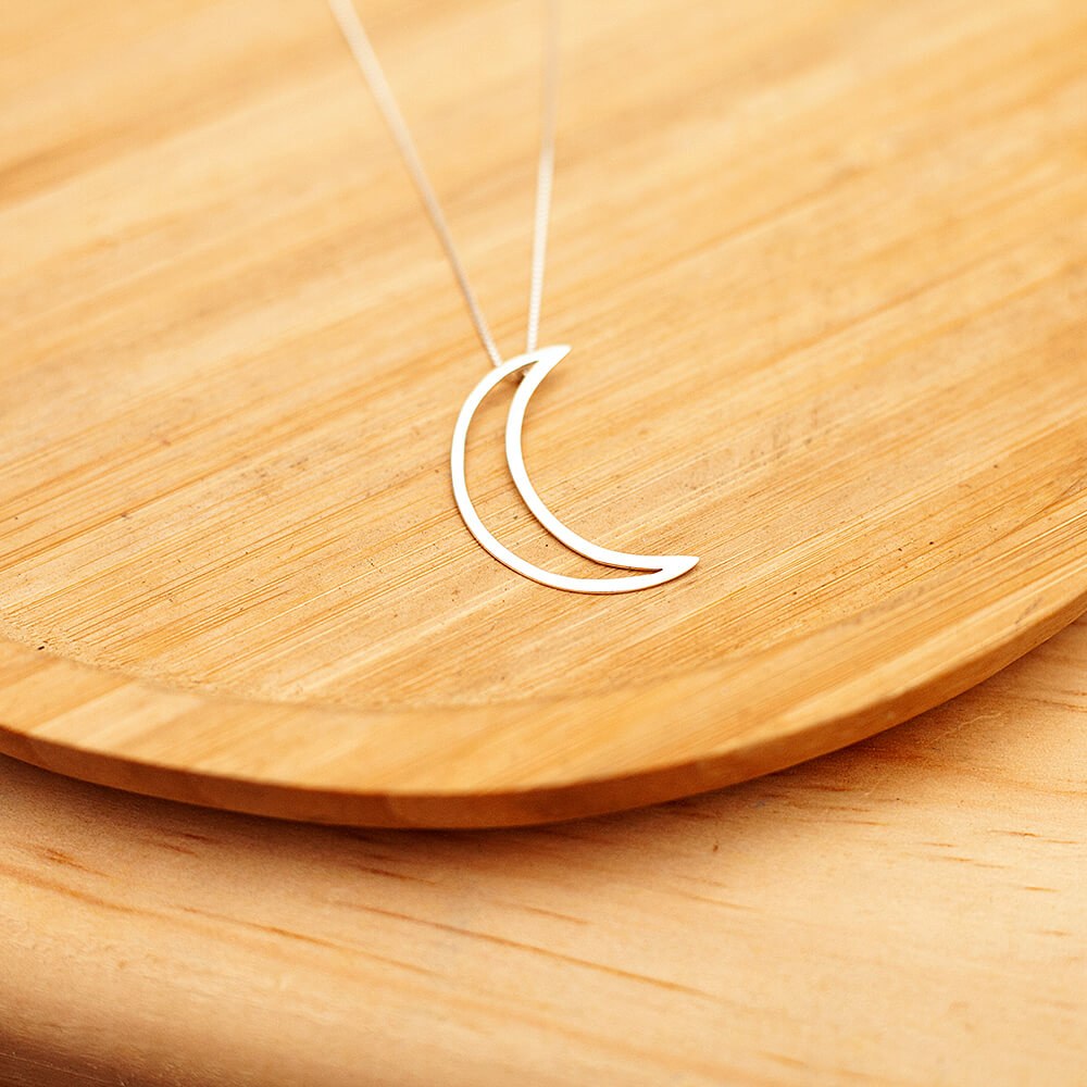 Foto do colar "Lua Vazada", acima de uma base de madeira rústica