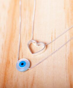 Foto do Escapulário Coração e Olho Grego, acima de uma base de madeira rústica
