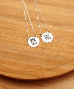 Foto do colar “Escapulário Ore por Mim”, acima de uma base de madeira rústica