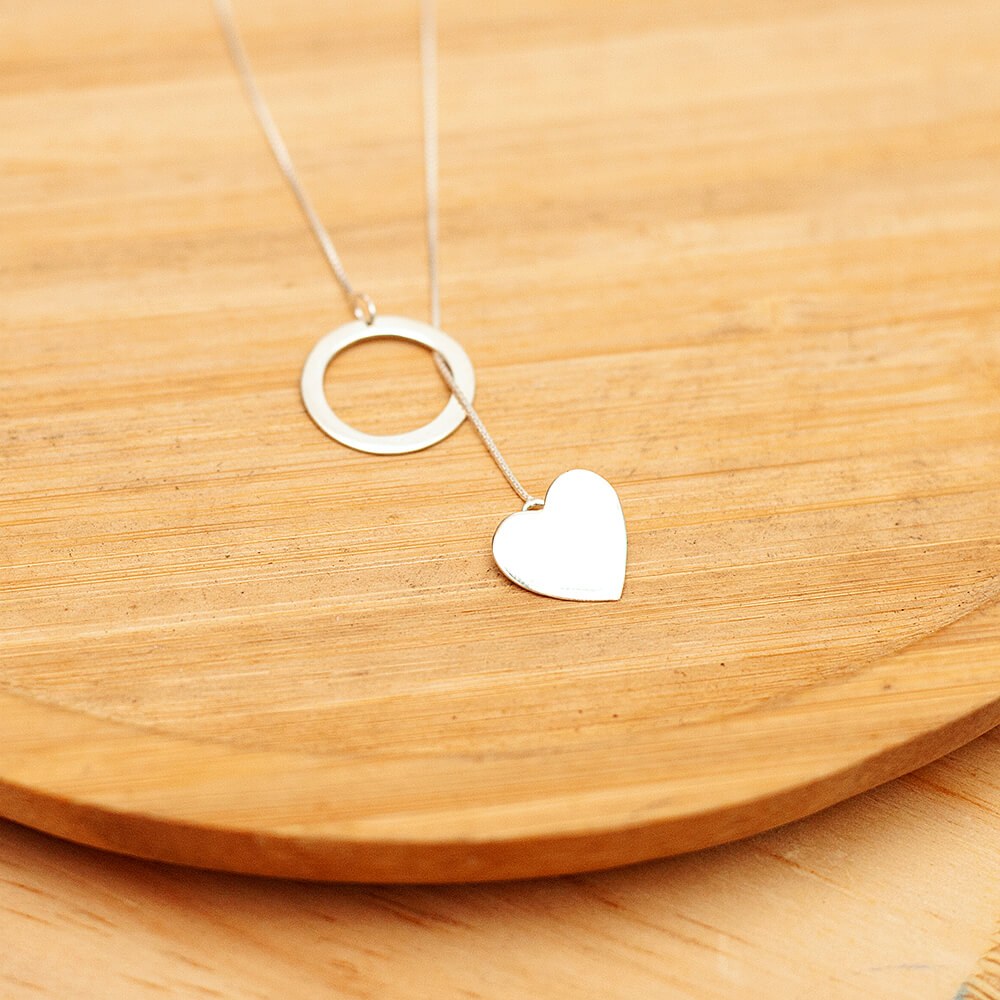 Foto do colar “Gravatinha Circulo e Coração”, acima de uma base de madeira rústica